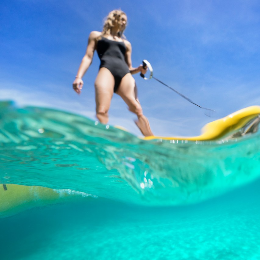 An underwater photo looking up at a blonde woman riding a yellow Lampuga Air jetboard