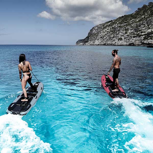 Two drivers, one male and one female, riding on their red and grey lampuga jetboards on crystal blue water.